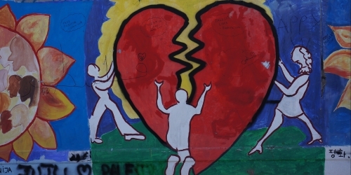 Grafitti on the Israeli security wall of a person kneeling, with upstretched hands, before a large, painted red heart that is broken in two. Its pathos is palpable.